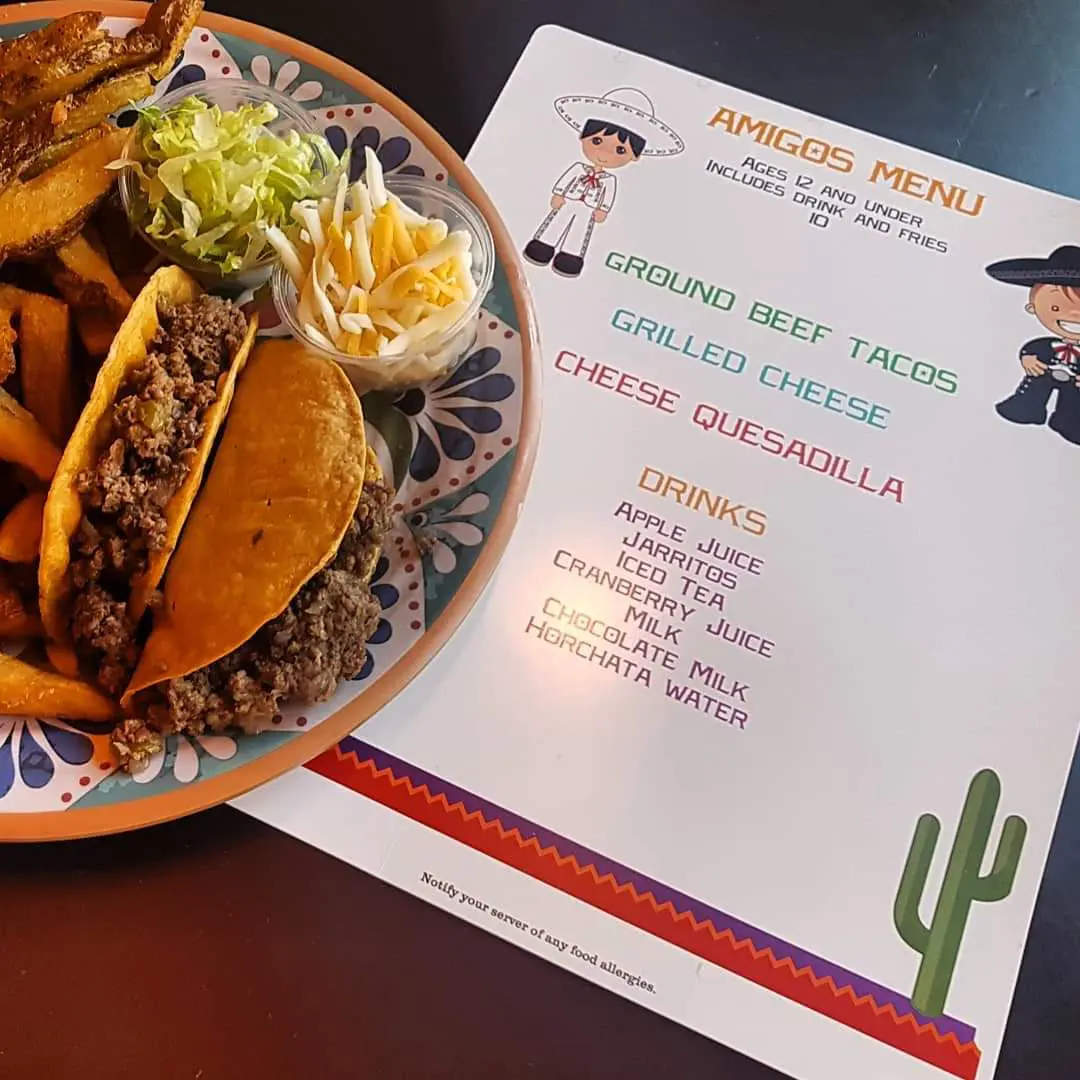 A Plate of Tacos and Fries Next to a Restaurant Menu